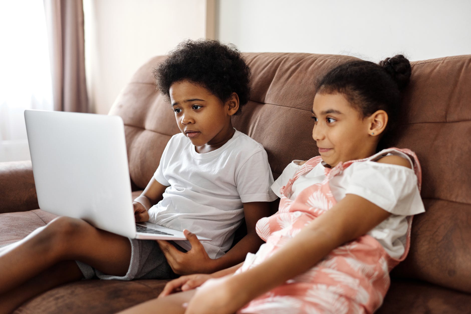 siblings sitting on a couch and looking at a laptop